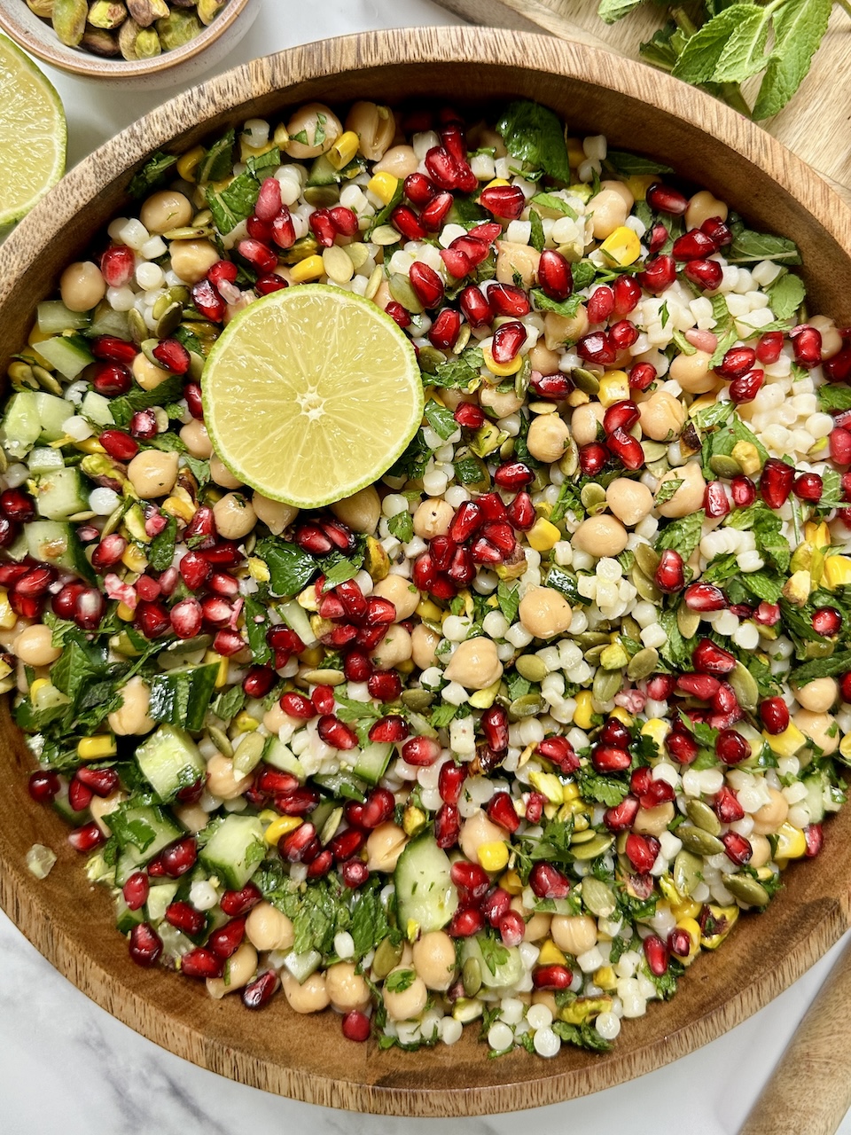 giant cous cous salad with pistachio, pomegranate and lime in a wooden bowl