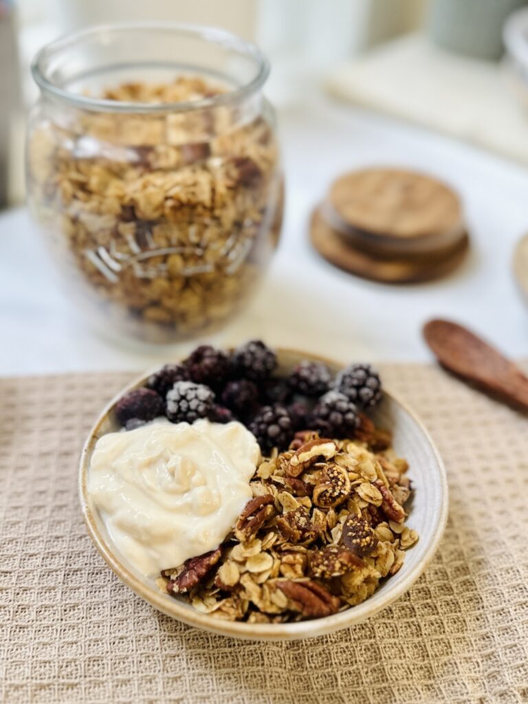 fig and pecan granola in bowl with blackberries and granola with yoghurt. jar of granola in background